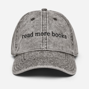 May include: A grey, vintage-style baseball cap with the phrase "read more books" embroidered in black. The cap has a curved peak and a distressed appearance, suggesting a worn look.