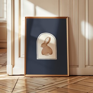May include: Framed art print featuring a watercolor illustration of a brown rabbit. The artwork is set against a navy blue background and framed in a gold-colored frame. The rabbit is depicted in a minimalist style.
