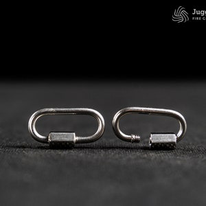 May include: Two silver-colored metal oval quick links, one closed and one open with a threaded screw gate mechanism. The logo Juggling Calling FIRE GEAR MANUFACTURER is visible in the top right corner of the image.