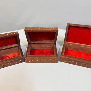 May include: Three wooden boxes with intricate inlaid designs and red velvet interiors. The boxes are nested inside each other, with the largest box at the bottom and the smallest box at the top.