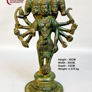 May include: A green metal statue of a Hindu deity with multiple heads and arms. The statue is standing on a decorative base and is holding a weapon in one hand. The statue is 30 cm tall, 20 cm wide, and 15 cm deep. It weighs 3.370 kg.