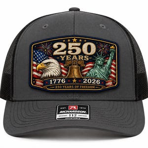Puede incluir: Una gorra tipo trucker gris carbón con un parche rectangular que incluye el texto 250 YEARS, 1776, 2026 y 250 YEARS OF FREEDOM. El parche muestra un águila calva, la Campana de la Libertad, la Estatua de la Libertad y una bandera de EE. UU.