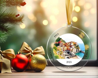 May include: A clear round Christmas ornament with a picture of a colorful Italian village on a cliff overlooking the ocean. The ornament has the text "Amalfi Coast" and "2024" printed on it. The ornament also has the names of Italian cities printed around the edge: "Rome", "Venice", "Sorrento", "Pisa".