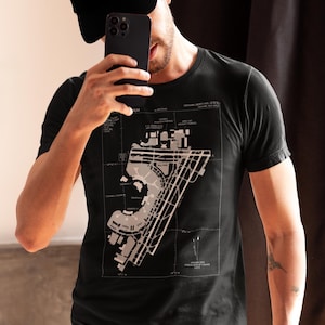 Puede incluir: Camiseta negra con un diagrama detallado del diseño de un aeropuerto en gris claro. El diseño incluye pistas, terminales y calles de rodaje. El texto es visible en la parte superior e inferior del diagrama. La camiseta está hecha de un material suave.