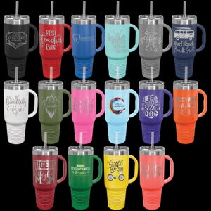 May include: A collection of insulated travel mugs in various colors, each with a handle, straw, and engraved text or graphics. Colors include black, red, blue, teal, gray, navy, white, olive green, pink, light blue, purple, and orange. Text includes "Vineyard", "Best Teacher Ever", and "Surf Shack Bar & Grill".