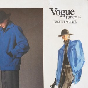 May include: A Vogue Patterns Paris Original sewing pattern envelope featuring a blue jacket with a collar, long sleeves, and pockets. The cover displays a photograph of the jacket worn with a black hat and gloves, alongside a fashion illustration.
