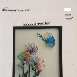 May include: An embroidery design titled "Loopy's Garden" features colorful, daisy-like flowers and a butterfly. The design includes the text "Millefiori Design #873". The color options are cream and white.