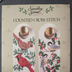May include: Counted cross stitch door knob decor set featuring chickadees and cardinals. The finished size is 5" x 12" each. The design includes a red cardinal and a brown cardinal, with the text "Something Special".