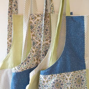 May include: Several fabric tote bags with long straps hang from hooks. The bags feature a variety of patterns, including blue floral, white polka dots, and green herringbone. The bags are made of cotton fabric and are likely for carrying groceries or other items.