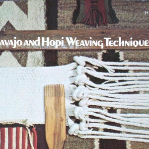 May include: A book titled Navajo and Hopi Weaving Techniques featuring a cover image of a wooden weaving comb resting on a white woven textile with long fringe, set against a background of a brown, black, and white patterned woven rug.