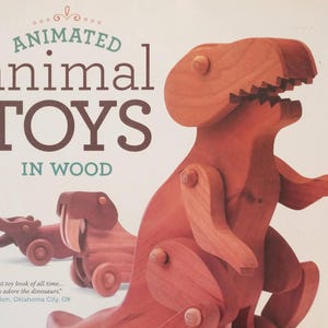 May include: A book titled ANIMATED animal TOYS IN WOOD featuring a large wooden dinosaur toy and a smaller wooden walrus toy on the cover. The cover includes the text: Greatest toy book of all time... the kids adore the dinosaurs. -Ron, Oklahoma City, OK.