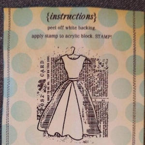 May include: A vintage-style postcard with instructions for a stamp. The card features a dress illustration and text that reads "{instructions}", "peel off white backing", and "apply stamp to acrylic block. STAMP!". The background is light yellow with blue polka dots.