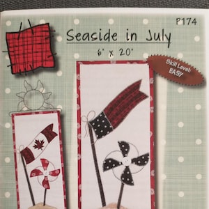 May include: A fabric panel with the text "Seaside in July" and dimensions of 6" x 20". The panel features patriotic flags and pinwheels with red, white, and blue patterns. The skill level is marked as "EASY".