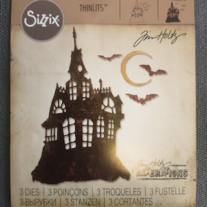 May include: A Sizzix Thinlits die set featuring a haunted house design with bats and a crescent moon. The set includes 3 dies and is part of the Jim Holtz Alterations collection. The packaging has a vintage, distressed look.