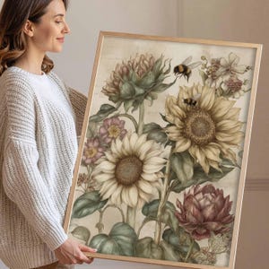 Puede incluir: Una impresi&oacute;n floral enmarcada con girasoles, otras flores y abejas. La obra de arte tiene una est&eacute;tica vintage con colores suaves, incluyendo crema, amarillo y verdes apagados. El marco de madera complementa el tema natural de la obra.