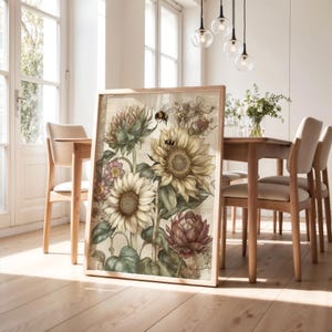 Puede incluir: Un estampado bot&aacute;nico enmarcado con girasoles, abejas y otras flores en tonos amarillos, verdes y morados. La obra de arte se exhibe en un marco de madera clara, en un comedor.