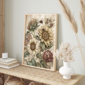 Puede incluir: Un estampado bot&aacute;nico enmarcado con girasoles, alcachofas y otras flores en tonos crema, amarillo y burdeos. Se representan dos abejas cerca de los girasoles. La obra de arte se exhibe en una pared de color claro.
