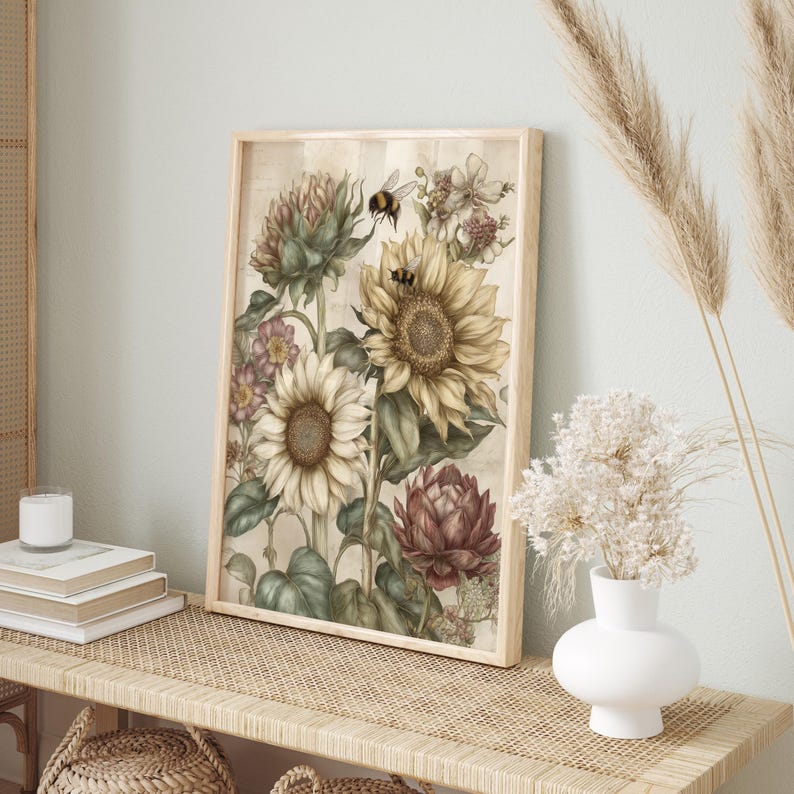 Puede incluir: Un estampado bot&aacute;nico enmarcado con girasoles, alcachofas y otras flores en tonos crema, amarillo y burdeos. Se representan dos abejas cerca de los girasoles. La obra de arte se exhibe en una pared de color claro.