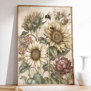 Puede incluir: Una impresi&oacute;n bot&aacute;nica enmarcada con girasoles, otras flores y abejas. La obra de arte tiene una est&eacute;tica vintage con colores suaves, incluyendo crema, amarillo, rosa y verde. La impresi&oacute;n est&aacute; en un marco de madera.