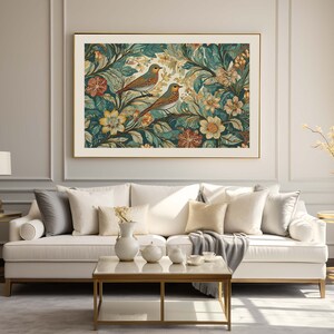 May include: A white sofa with gold legs and a gray throw blanket sits in front of a framed print of birds and flowers. The print has a gold frame and is hung on a white wall with gold trim.
