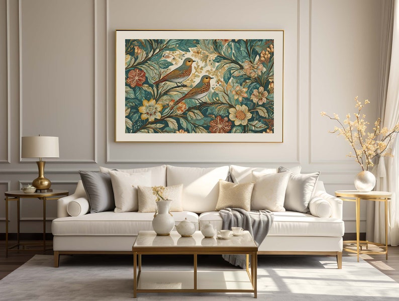 May include: A white sofa with gold legs and a gray throw blanket sits in front of a framed print of birds and flowers. The print has a gold frame and is hung on a white wall with gold trim.