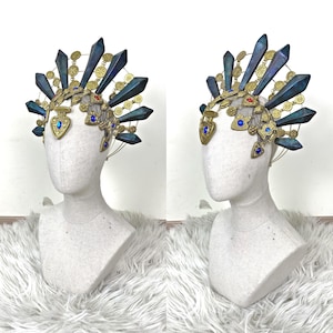 May include: A decorative headpiece featuring a gold-toned metal frame adorned with dark blue, pointed, crystalline-shaped spikes. The structure includes small gold circular medallions, heart-shaped charms with blue and red gems, and a wire base.