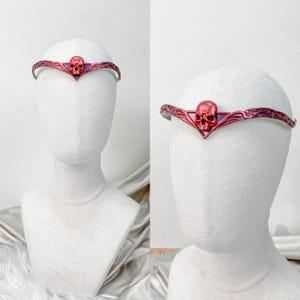 Puede incluir: Un tocado de calavera roja con un diseño decorativo. El tocado está hecho de metal y tiene un acabado rojo oscuro. Es un accesorio tipo corona.