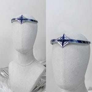 Puede incluir: Una diadema plateada con un diseño de estrella azul y plateada. La diadema se lleva en una cabeza de maniquí blanca.