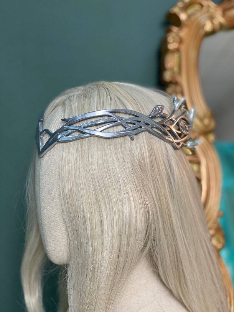 Puede incluir: Una corona plateada con un dise&ntilde;o delicado e intrincado. La corona est&aacute; hecha de metal y tiene un patr&oacute;n de hojas. Se lleva en un maniqu&iacute; con cabello rubio.