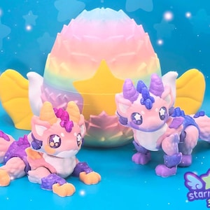 May include: Two articulated dragon figures in pink, purple, and blue hues, with star-shaped eyes, are displayed in front of a pastel-colored egg-shaped structure. The background is a gradient blue with star accents. The logo "starmouse 3D" is visible.