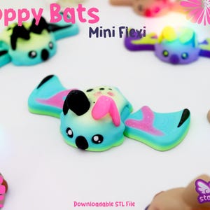 May include: Colorful, miniature bat figurines with outstretched wings. The bats are primarily blue, with accents of pink, yellow, and black. The text "Floppy Bats" and "Mini Flexi" are visible. The figurines are likely 3D printed.