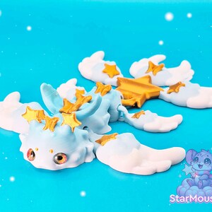 May include: A light blue and white articulated dragon toy with gold stars. The dragon has wings and a long tail. The toy is posed with its wings spread out.