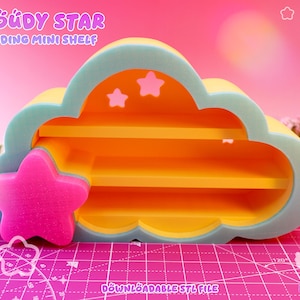 Op de afbeelding: Een wolkvormig staand minischapje met een lichtblauwe buitenrand, een feloranje binnenkant met twee horizontale planken en een opvallende roze ster aan de linkerkant. De tekst CLOUDY STAR STANDING MINI SHELF is zichtbaar.