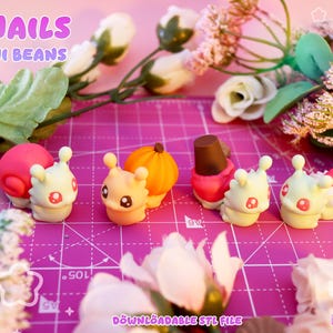 Può includere: Quattro piccole statuette di lumache con gusci distinti, tra cui una spirale rosa, una zucca arancione, un cono gelato marrone e una fragola rossa. Il testo recita SNAILS MINI BEANS e DOWNLOADABLE STL FILE. Le figure hanno corpi bianchi.