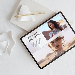 May include: A digital tablet displaying a webpage with the text "Iridescent Light Goddess" and images of a woman in desert scenery. A gold pen rests on a white ceramic shape, with additional white ceramic pieces nearby.