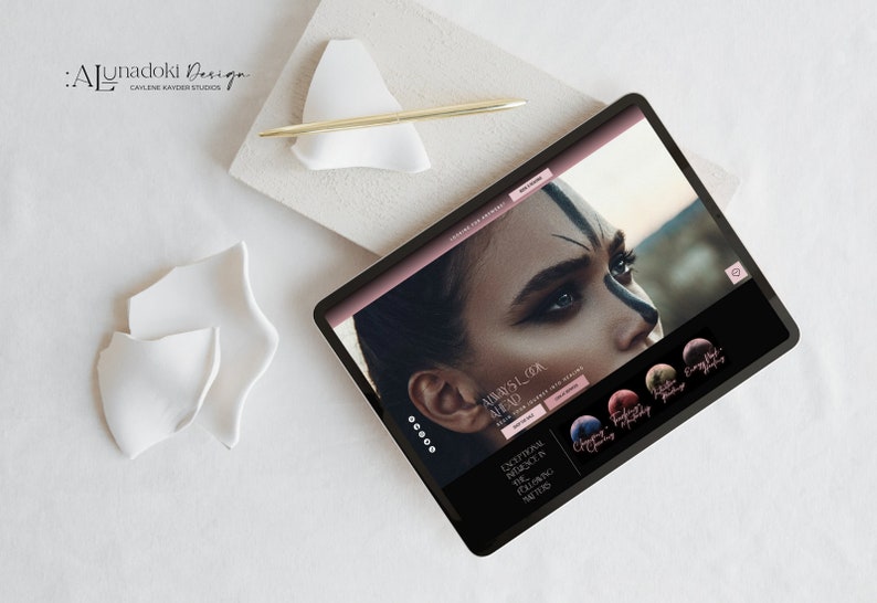 May include: A tablet computer displaying a website for a design studio called "Lunadoli Design." The website features a close-up image of a woman's face with dramatic makeup and the text "Always Look Ahead." The website also includes a section titled "Exceptional Muse in the Following Matter."