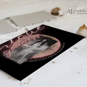 May include: A black card with pink and white text that reads "unique goddess" and "Live your life as you have always known you are magical". The card features a photo of a woman in a white dress with a pink moon behind her.