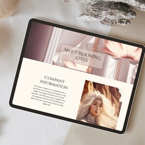 May include: A tablet displaying a website with the text "About Blooming Lotus" and "Company Information." The website features a photo of a woman with long white hair and a pink floral design. The tablet is on a neutral-toned surface.