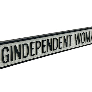 May include: A black and white sign with the text "Gindependent Woman" in black letters. The sign has a distressed, vintage look.