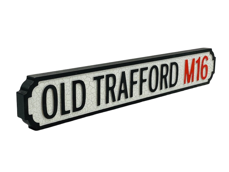 May include: Black and white street sign with the text "OLD TRAFFORD M16" in red letters.