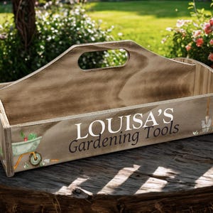 May include: Wooden gardening tool caddy with a handle. The caddy is painted with a distressed wood grain finish and features the text "LOUISA'S Gardening Tools". Decorative images of gardening tools and a wheelbarrow are also present.