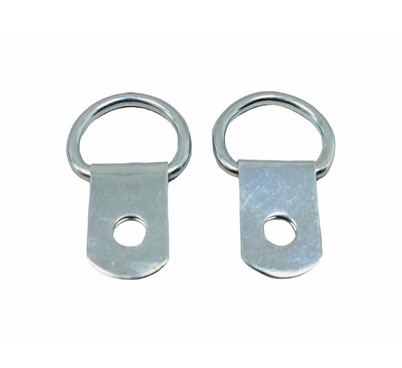 May include: Two silver metal D-ring picture hangers with a screw hole in the center of the flat base.
