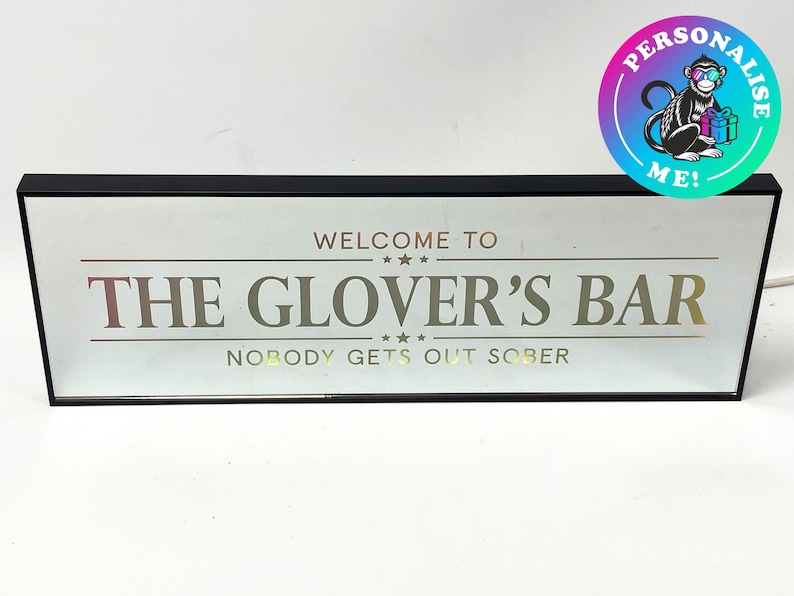 May include: A black framed sign with a white background and gold lettering that reads "Welcome to The Glover's Bar Nobody Gets Out Sober".
