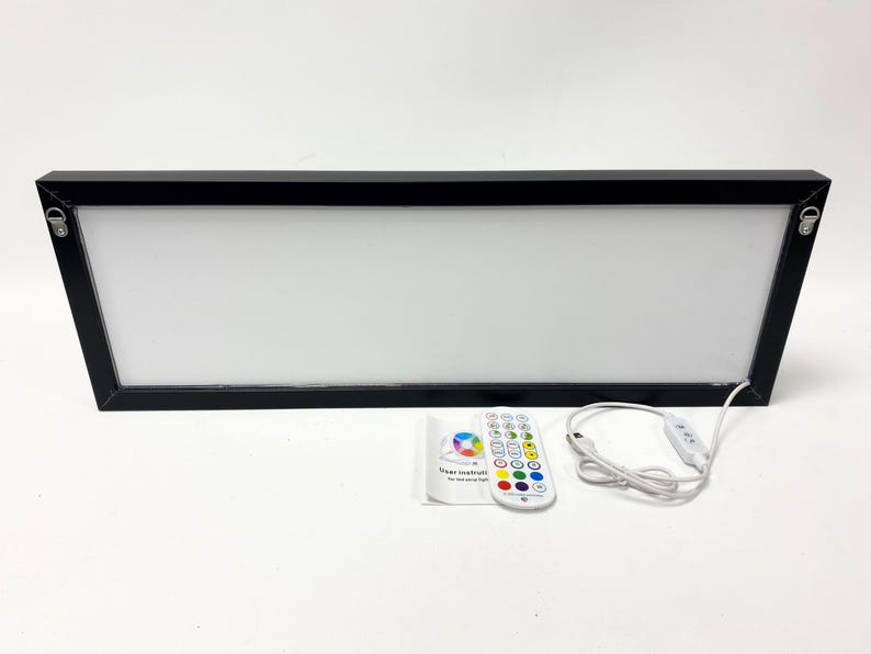 May include: A black framed light box with a white surface and a remote control. The remote control has a variety of color buttons and a power button. The light box is connected to the remote control by a white cord.