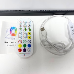 May include: A white remote control with a variety of buttons, including speed, mode, and color options. The remote control has a 2.4G music controller label and is connected to a white USB cable and a white receiver with the word "MOGA" printed on it.