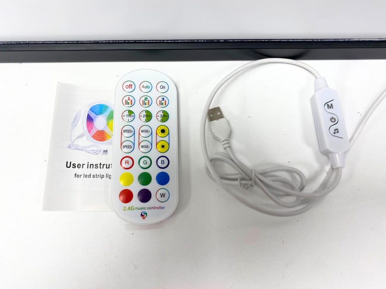May include: A white remote control with a variety of buttons, including speed, mode, and color options. The remote control has a 2.4G music controller label and is connected to a white USB cable and a white receiver with the word "MOGA" printed on it.