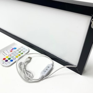 May include: A black framed light box with a white surface and a remote control. The light box is connected to a USB cable and has a switch to turn it on and off. The remote control has buttons for different colors and brightness levels. The light box is a great way to add a touch of color to any room.
