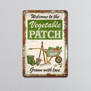 May include: A rectangular metal sign with a distressed, rusty brown border. The sign features the text "Welcome to the Vegetable Patch" in green and white, along with illustrations of gardening tools and a wheelbarrow filled with vegetables. The words "Grown with love" are at the bottom.