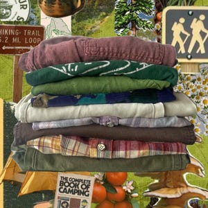 May include: A collage featuring a stack of folded shirts in various colors, including green, brown, and plaid. The image includes camping-themed elements like a campfire, a Smokey Bear badge, and a sign that says "Welcome to Colorful Colorado."