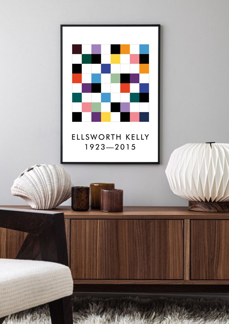 May include: A black framed print with a colorful geometric pattern and the text "ELLSWORTH KELLY 1923-2015". The print is hanging on a light gray wall above a wooden cabinet.